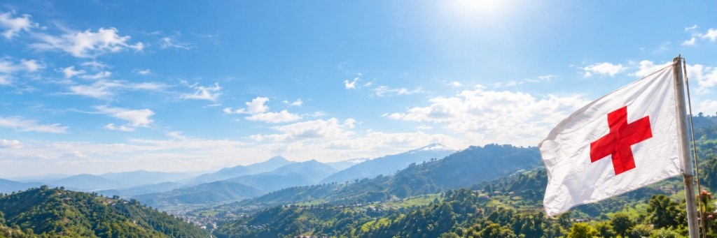 A Red Cross flag flying over green hills under a blue sky